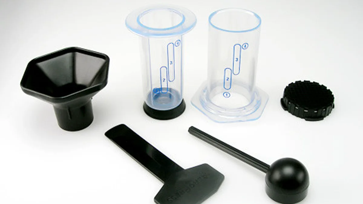 Barista hands pressing down the plunger of an AeroPress coffee maker into a sturdy ceramic mug