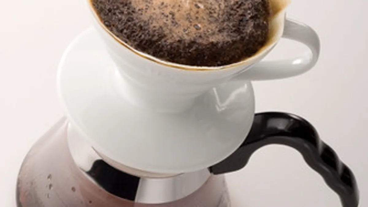 White ceramic Hario V60 dripper with spiral interior ribs resting on a glass server during pour over
