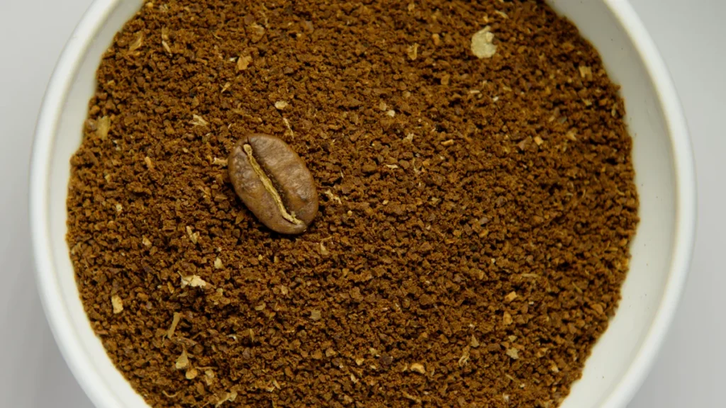 A small ceramic bowl displaying coarse coffee grounds with chunky sea salt texture next to roasted beans