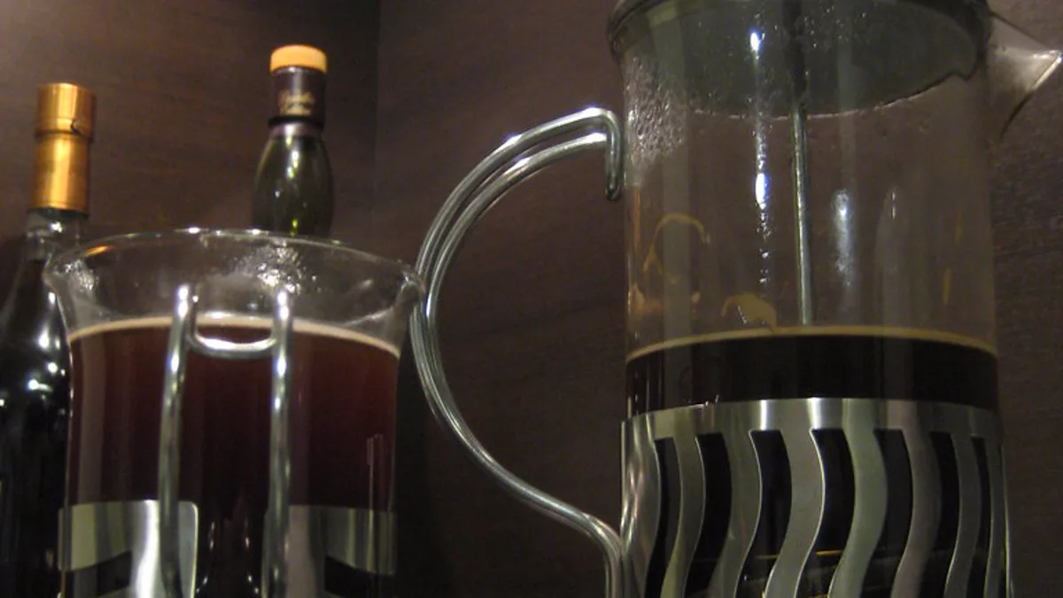 A glass French press filled with blooming coffee slurry showing coarse particles floating naturally