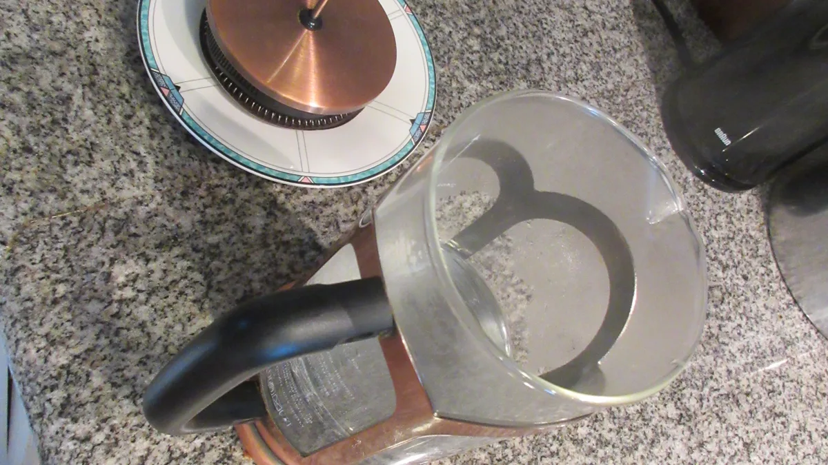 A hand gently pressing down the metal mesh plunger on a French press coffee maker