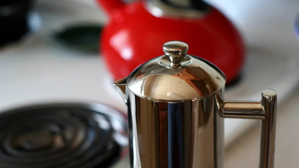 A glass French press carafe filled with rich dark coffee next to a ceramic pour over dripper
