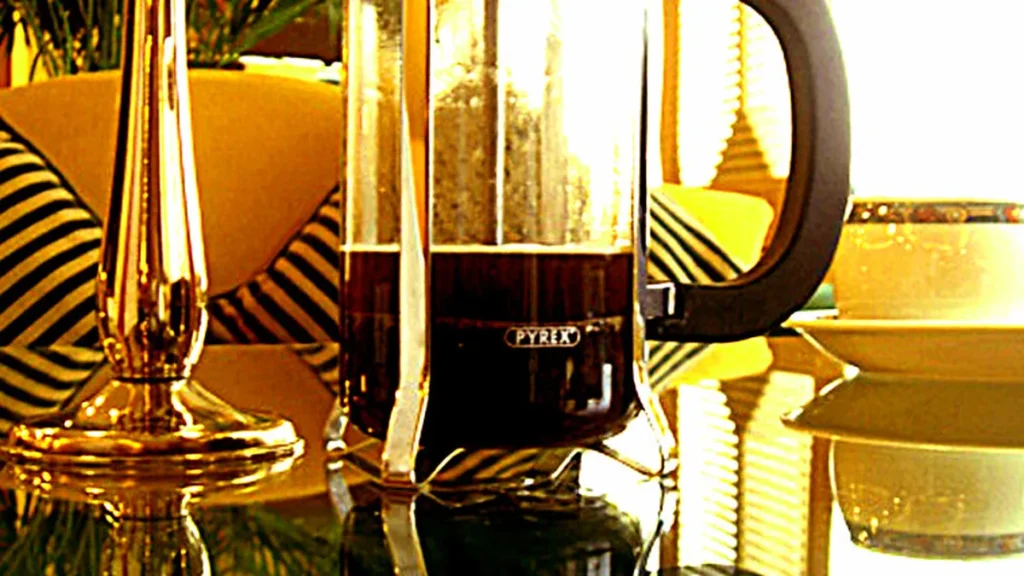 Steaming hot water pouring steadily from a ceramic teapot into a cup of loose leaf green tea leaves