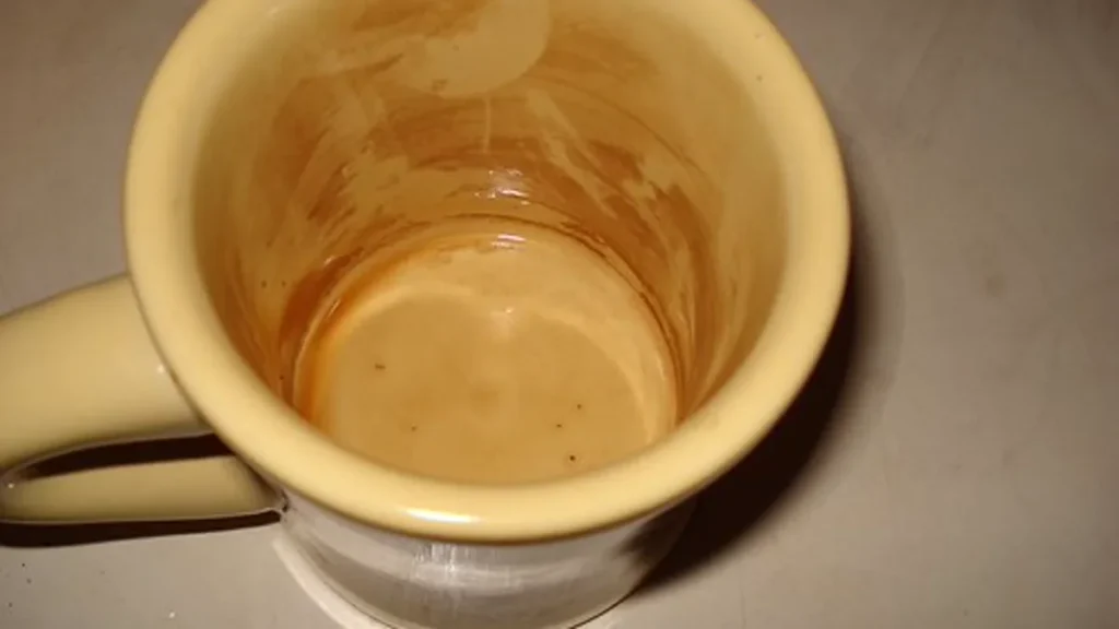 A barista using a stiff natural bristle brush to clean retained coffee grounds from an open conical burr assembly